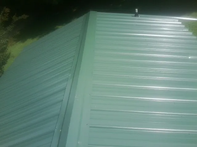 New green metal panels meeting at the ridge of a roof — Flat Roof Repair work by our crew in Worthington