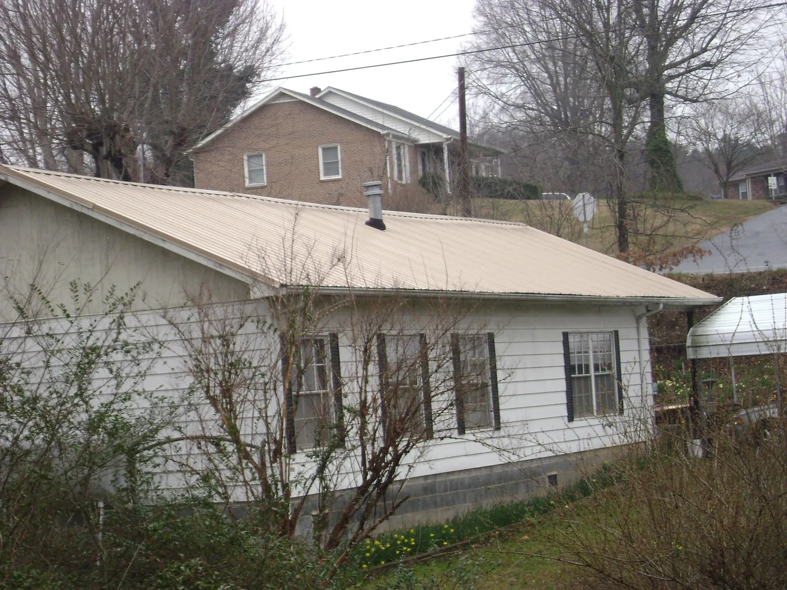 Tan metal roof on a white sided house set into a hillside — Commercial Roofing by Roofing Brothers in Worthington
